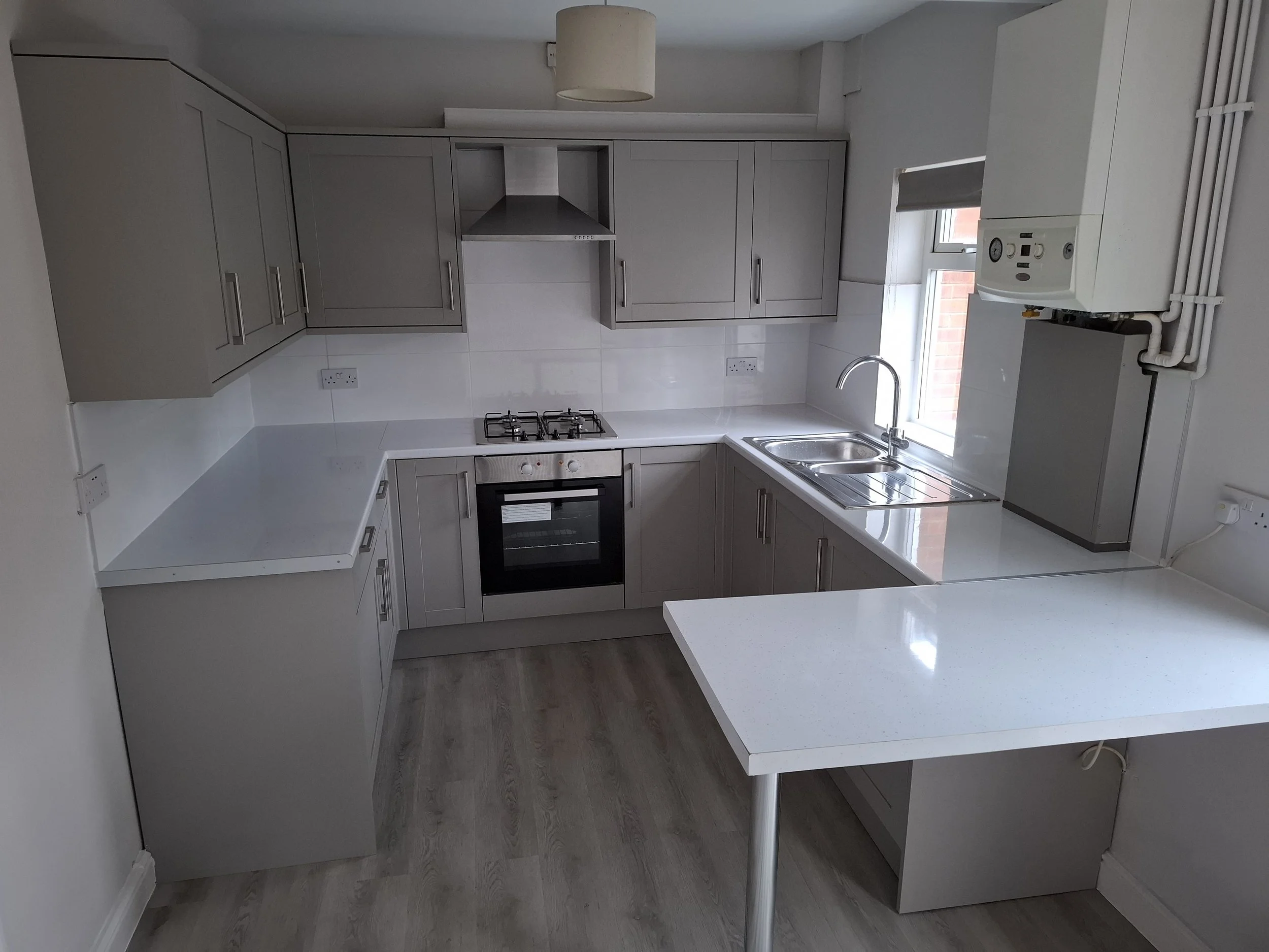 Modern kitchen with gray cabinets, stainless steel oven, gas cooktop, and a small window above the sink.