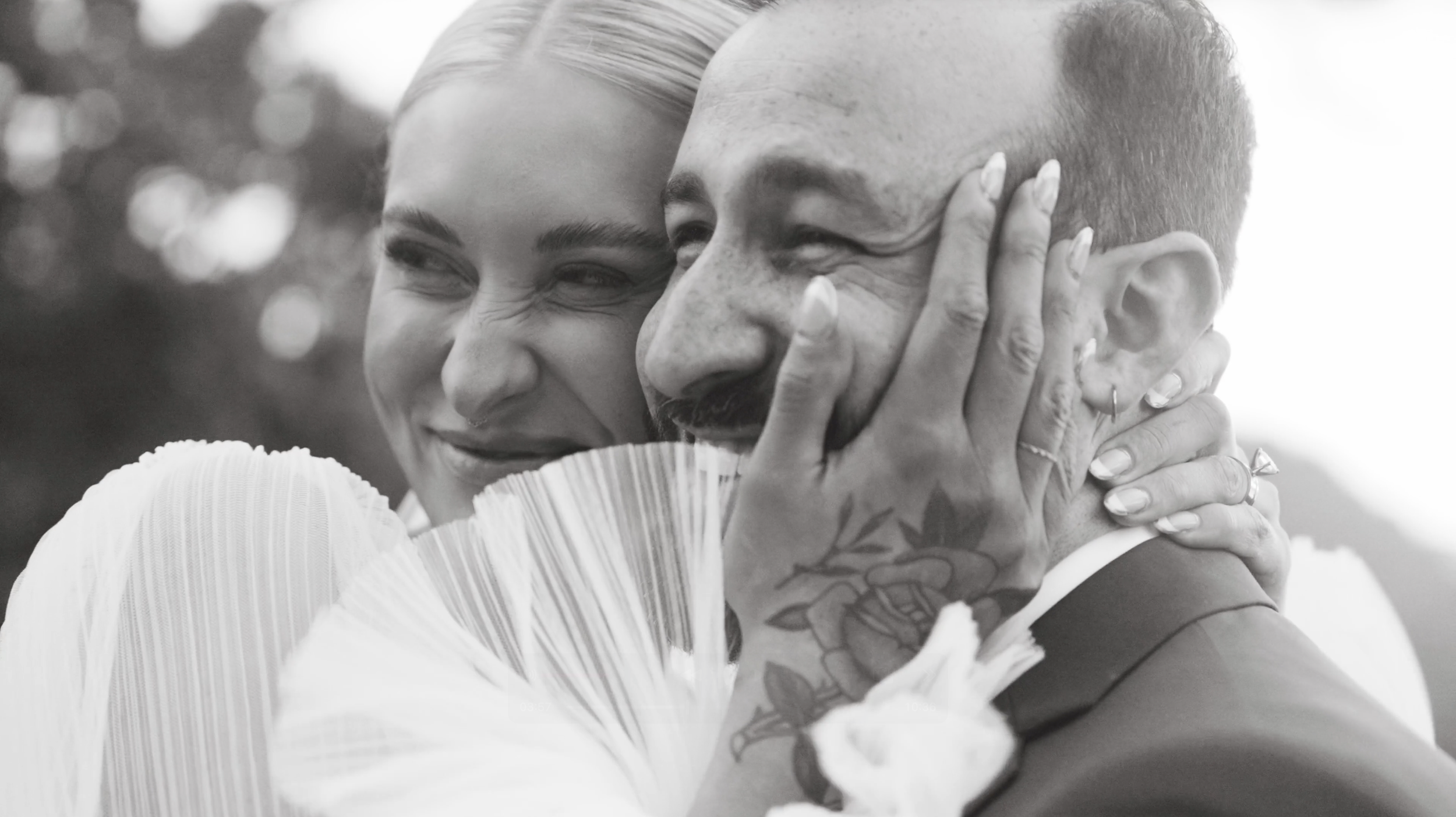 A black and white photo of a woman hugging a man tightly with a big smile on her face. She is holding his face with both hands, and they both appear joyful.