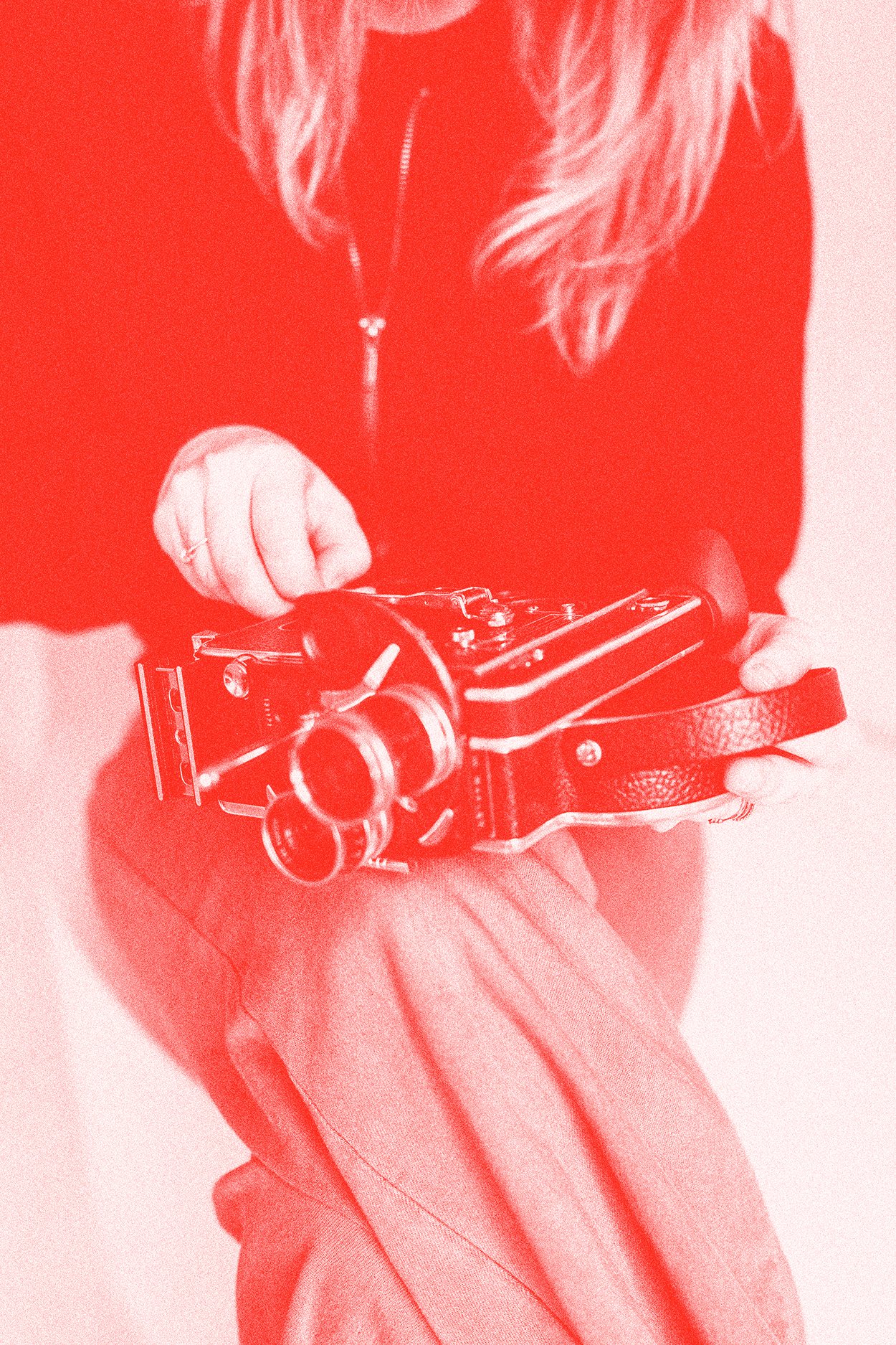 A person dressed in a dark jacket and light-colored pants is holding a vintage film camera, with their focus on the camera.