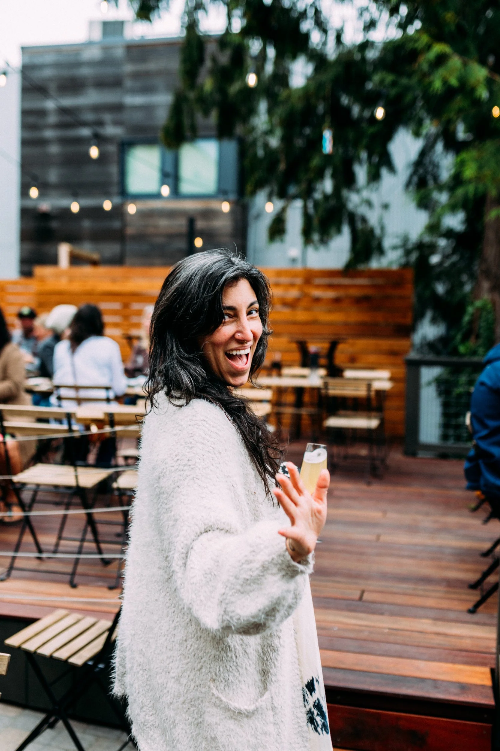 Woman smiling and waving with wine glass in hand