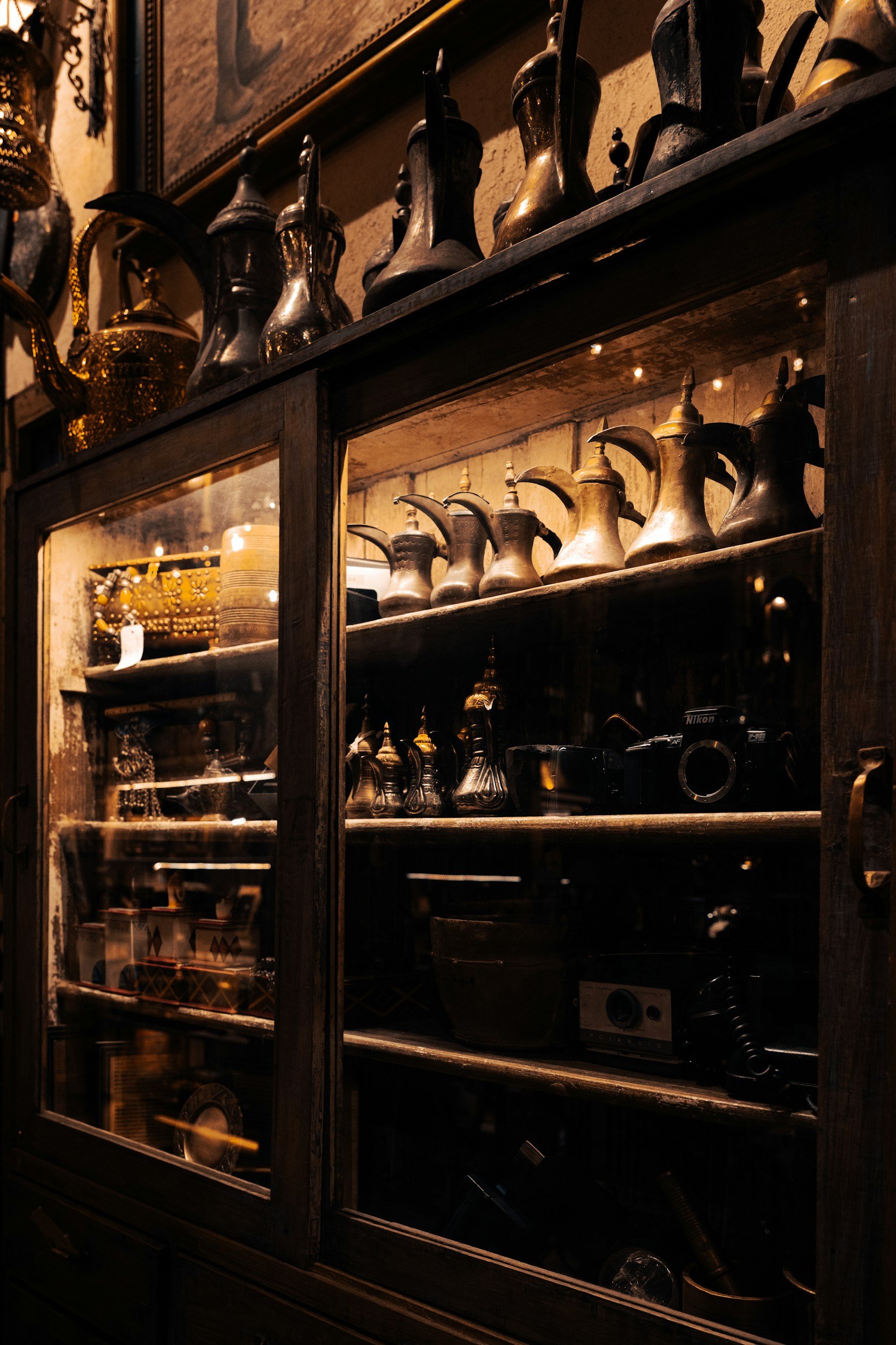 Vetrina di legno con oggetti d'antiquariato e teiere in modo vintage, alcune visibili attraverso le ante di vetro