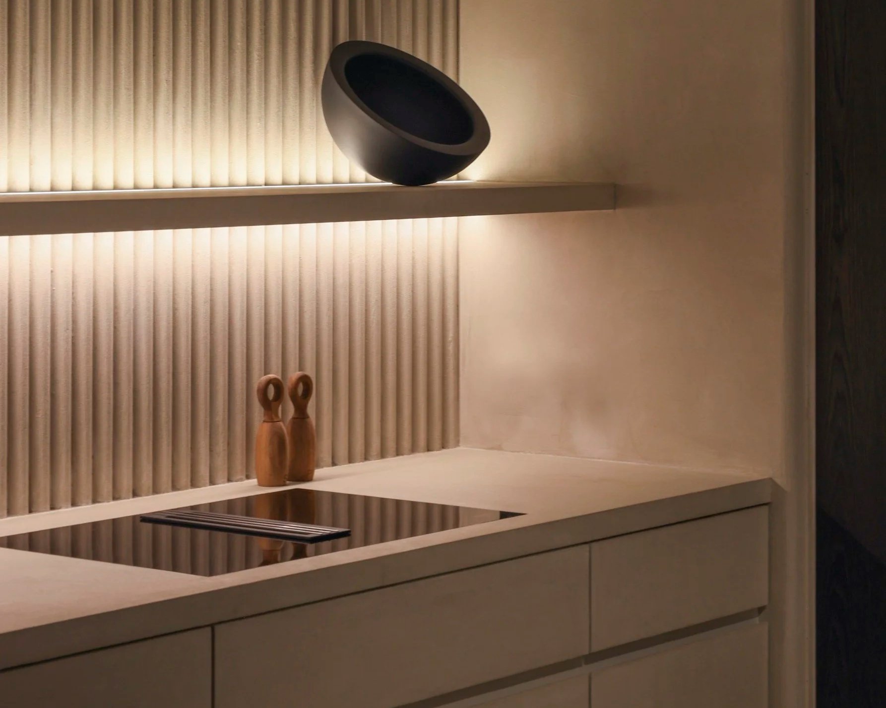 Cucina minimalista con piani chiari, decorazioni in legno e una lampada nera sospesa.