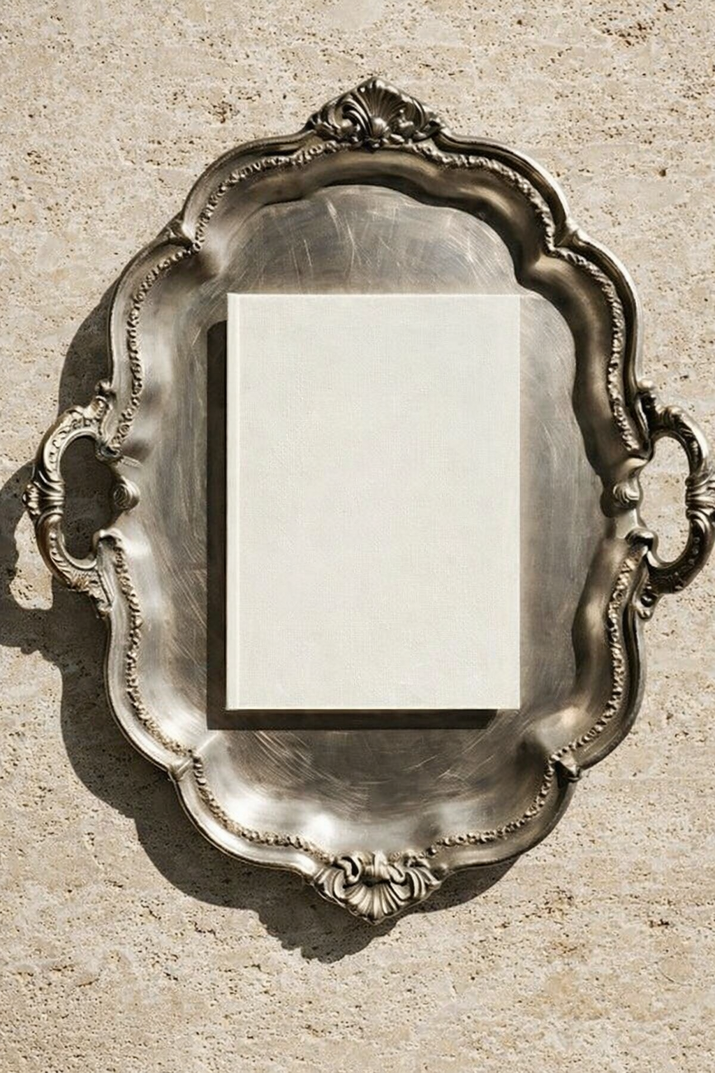Quadrato bianco su un piatto d'argento decorato con motivo barocco, posto su una superficie di pietra beige.