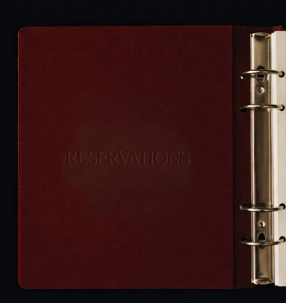 A red hardcover reservation book with the word "RESERVATIONS" embossed on the cover, attached to a metal ring binder.