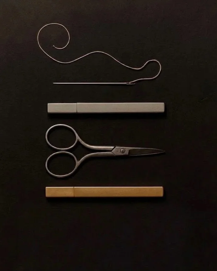 Set di oggetti disposti su uno sfondo nero, tra cui un ago, un tagliaunghie, due barre di metallo (bianca e beige) e una spilla con filo di metallo.