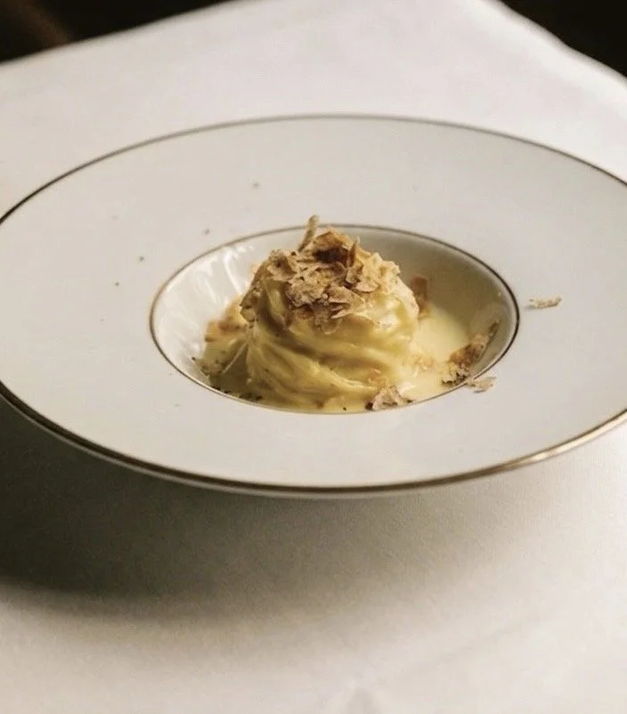 Piatto con una quenelle di paté decorato con scaglie di prosciutto, servito in una ciotola bianca con bordo dorato.