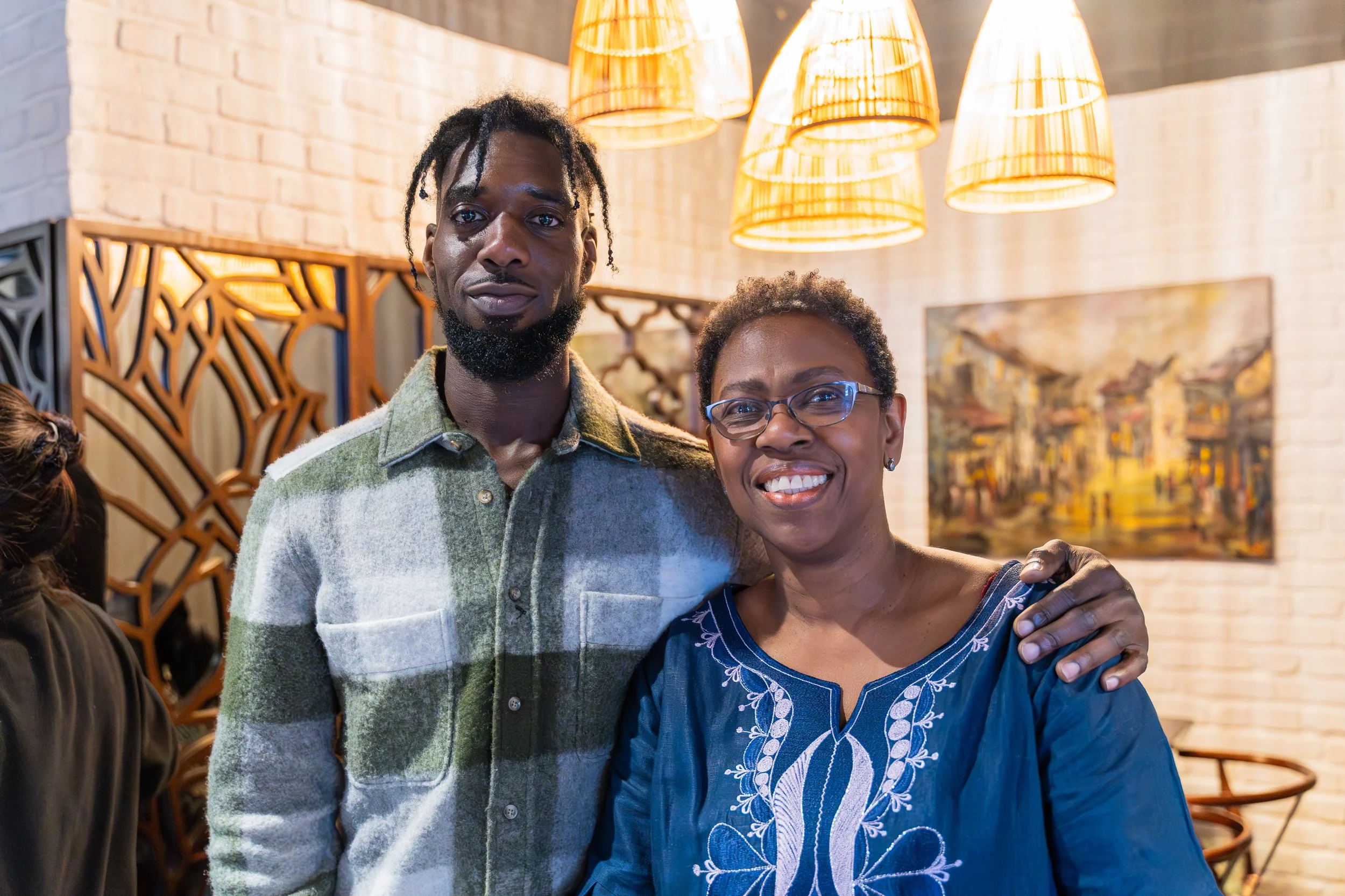 A man and woman smiling and embracing in a warmly lit restaurant with hanging pendant lights and artwork on the wall.