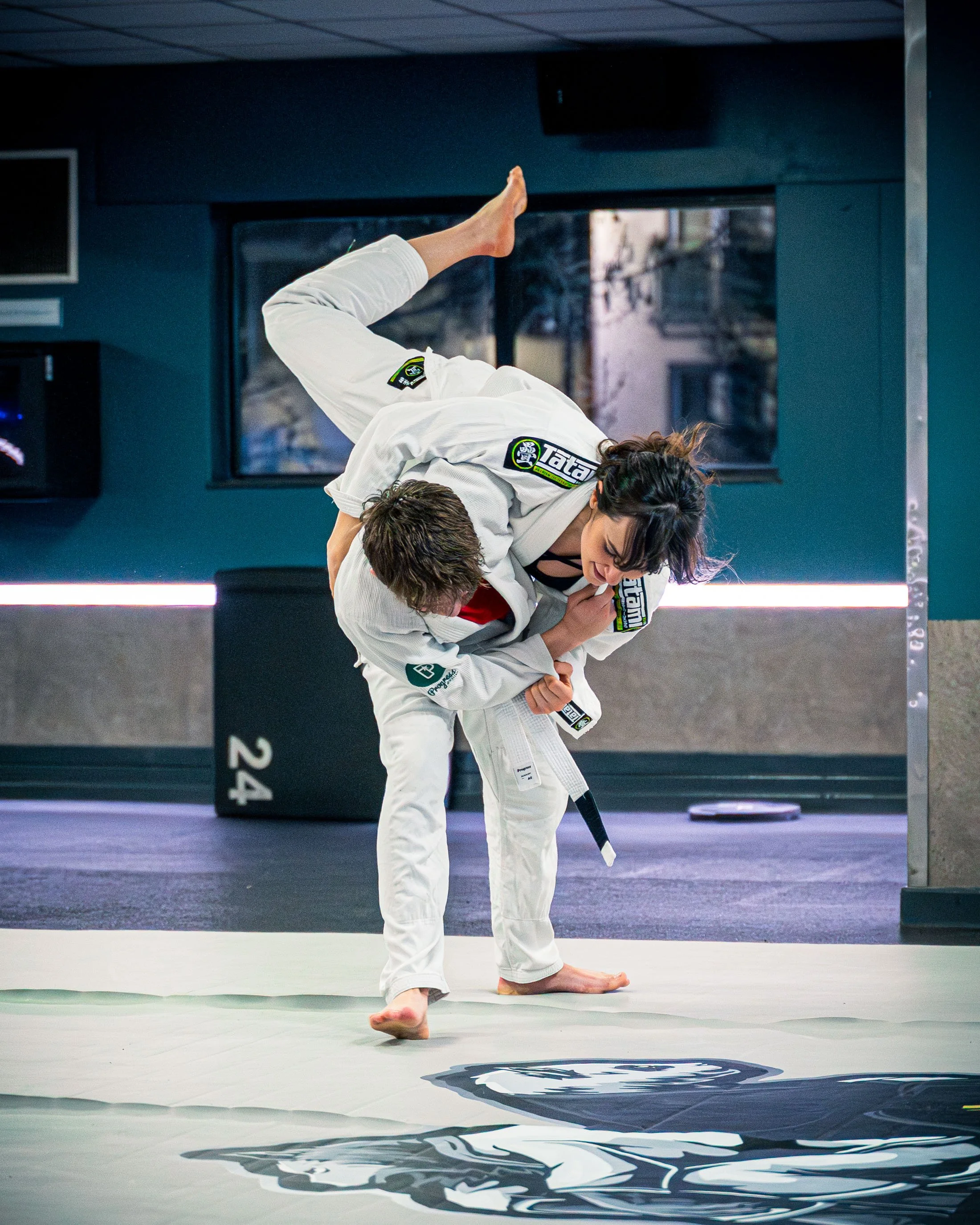 Two women practicing Brazilian Jiu-Jitsu on a mat. One woman is executing a throw, lifting the other woman off the ground.