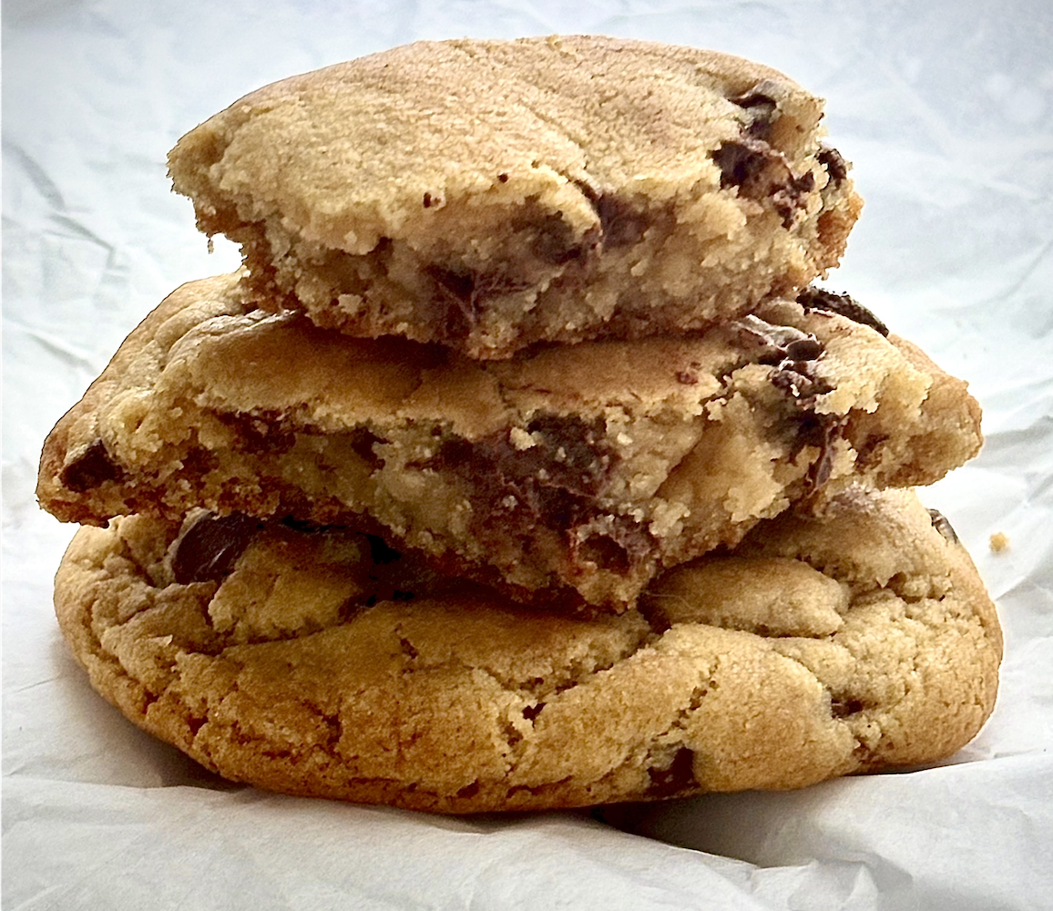 Stack of three chocolate chip cookies on white wrapping paper.