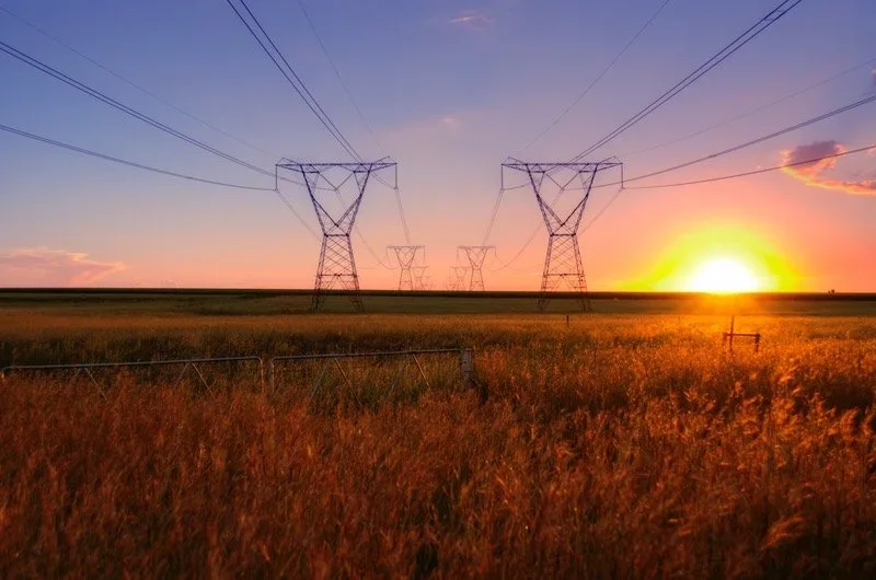 Power lines in a field with the sun