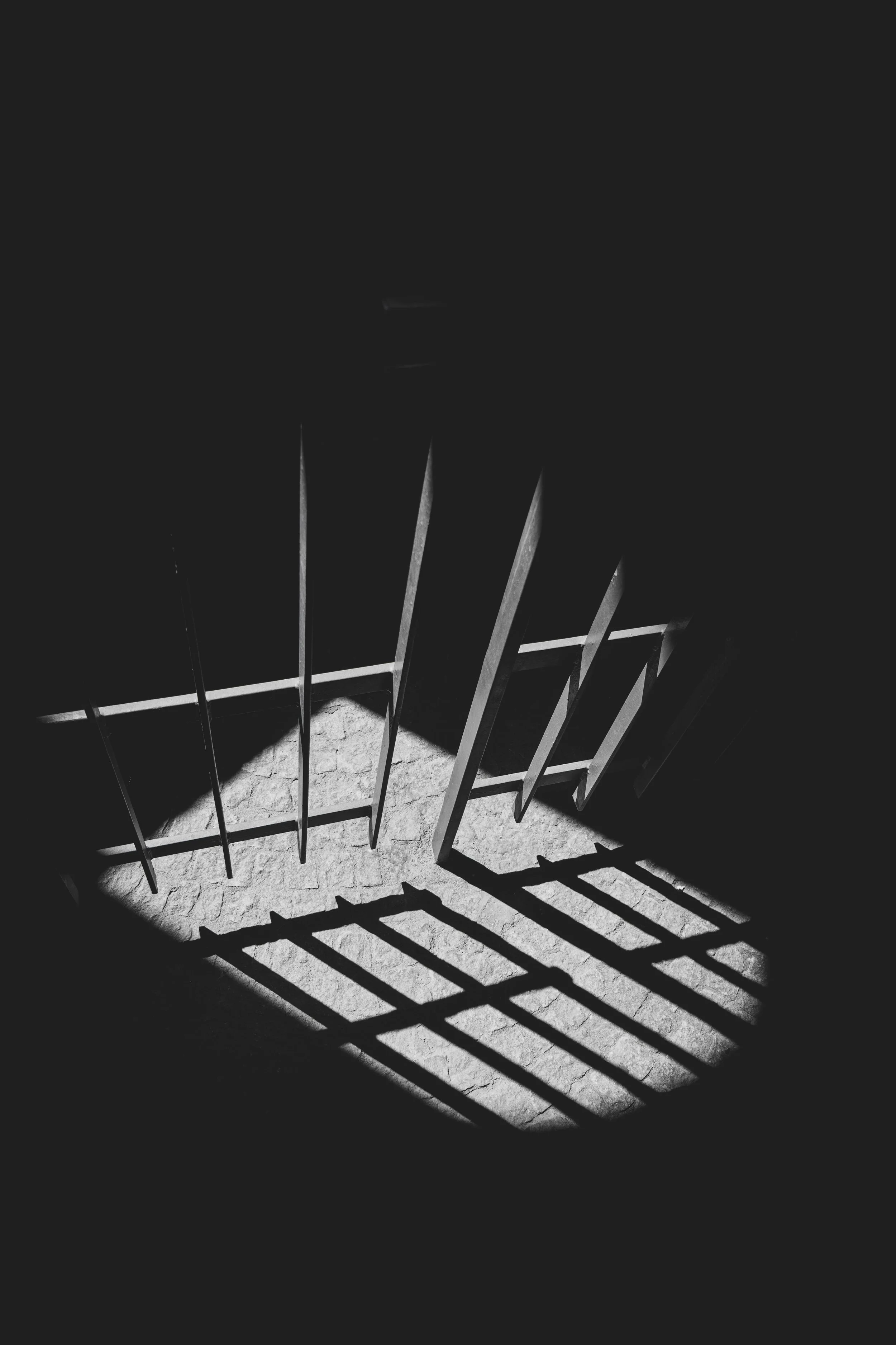 Shadows of metal bars cast on a stone floor in black and white.