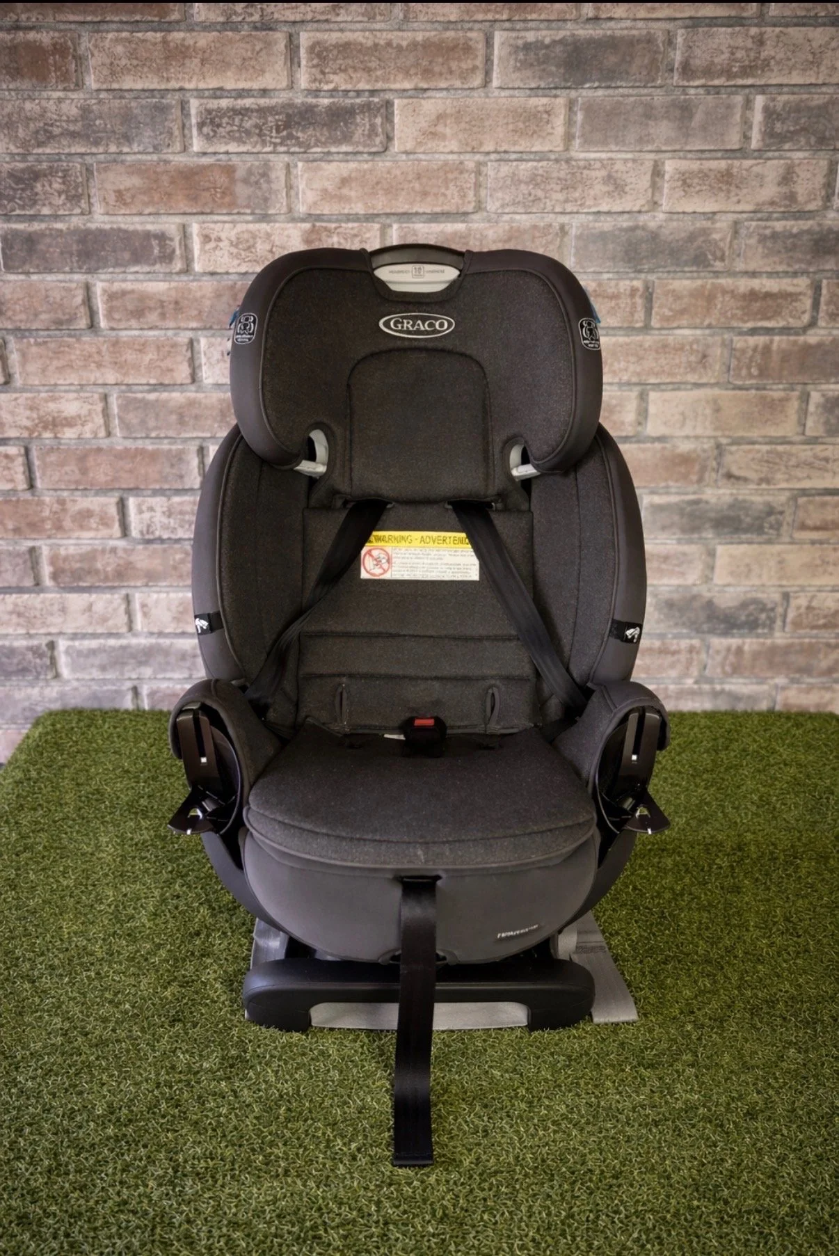 A black Graco child car seat on green carpet in front of a brick wall.