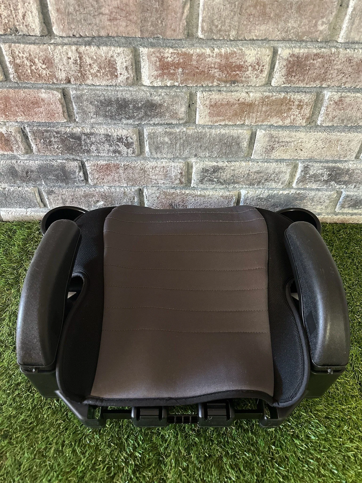 Child car seat placed on artificial grass in front of a brick wall.