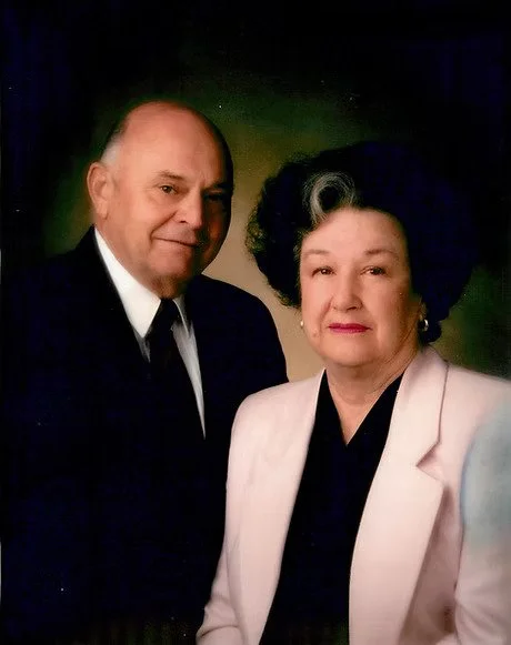 Ed and Shirley Bews portrait, both dressed formally, against a dark background.