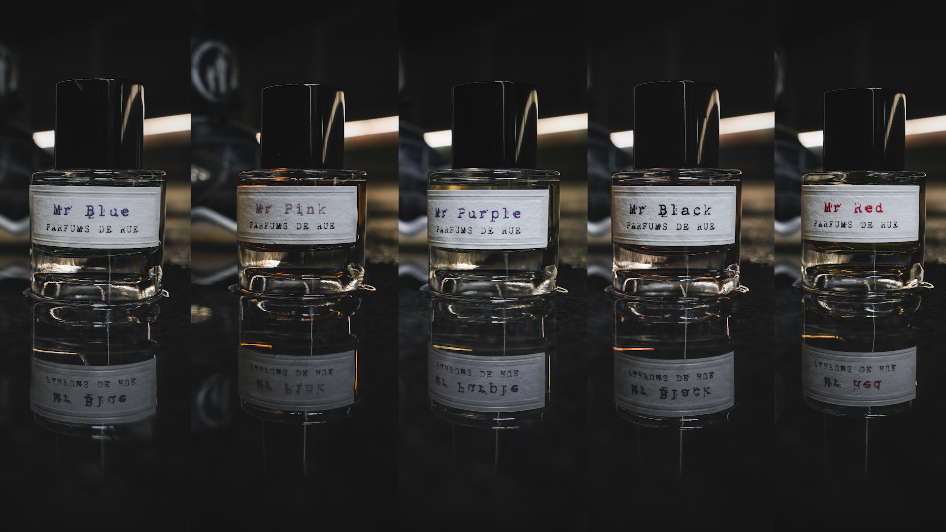 Cinq flacons de parfum sur une surface noire, chacun avec une étiquette indiquant la couleur : Mr Blue, Mr Pink, Mr Purple, Mr Black, Mr Red