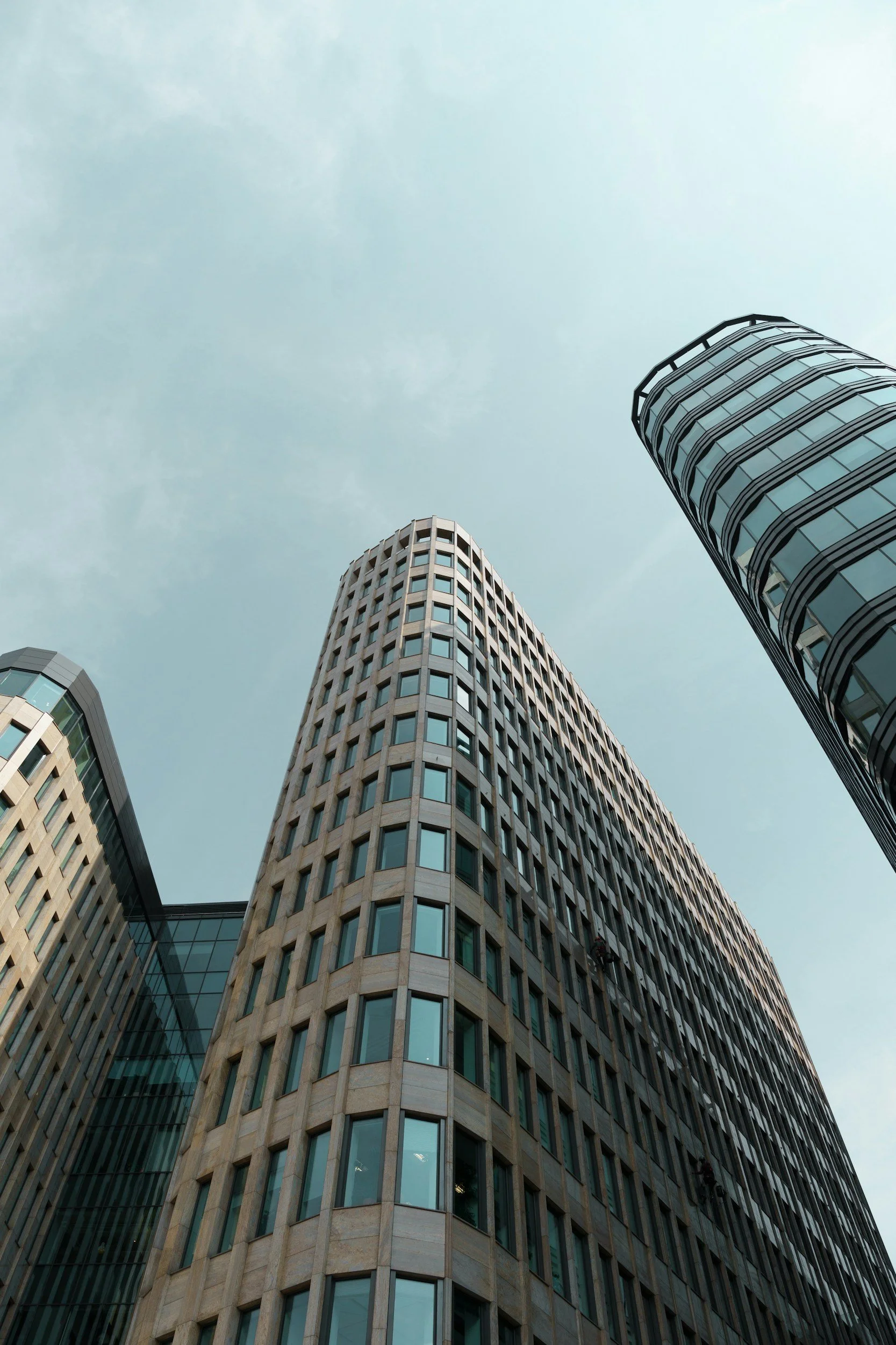 Low angle view of modern skyscrapers with glass windows and beige stone facades against a cloudy sky.