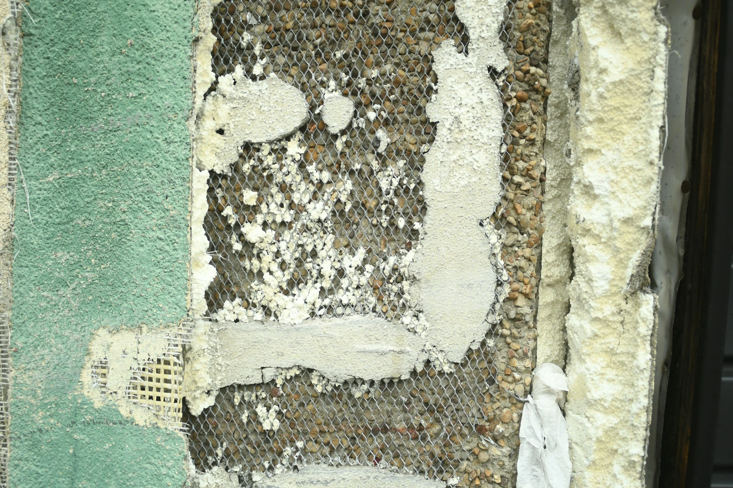 Close-up of a wall section with various insulation materials including foam, gravel, and spray foam, covered with a metal mesh.