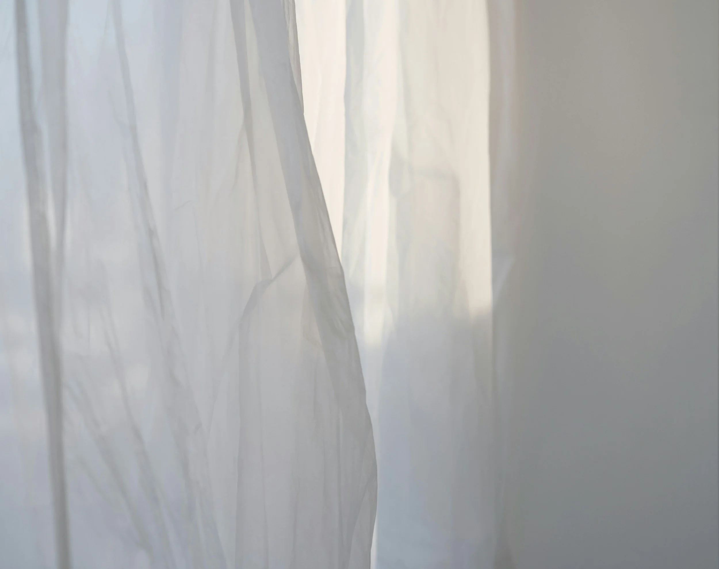 Close-up of semi-transparent white curtains with soft natural light filtering through.