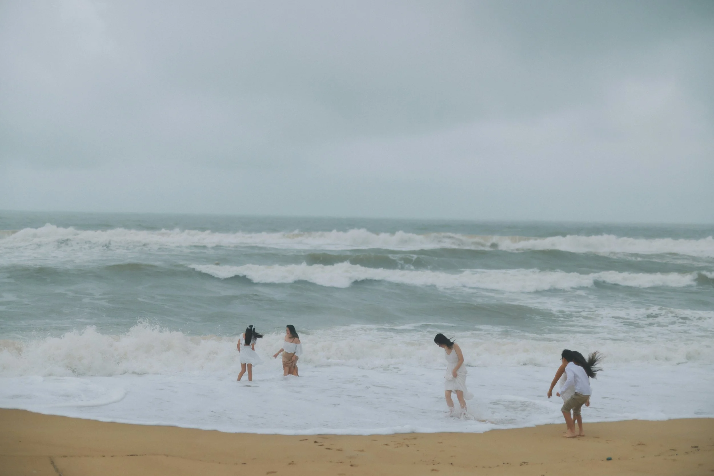 Four children playing in the ocean waves on a cloudy day at the beach.