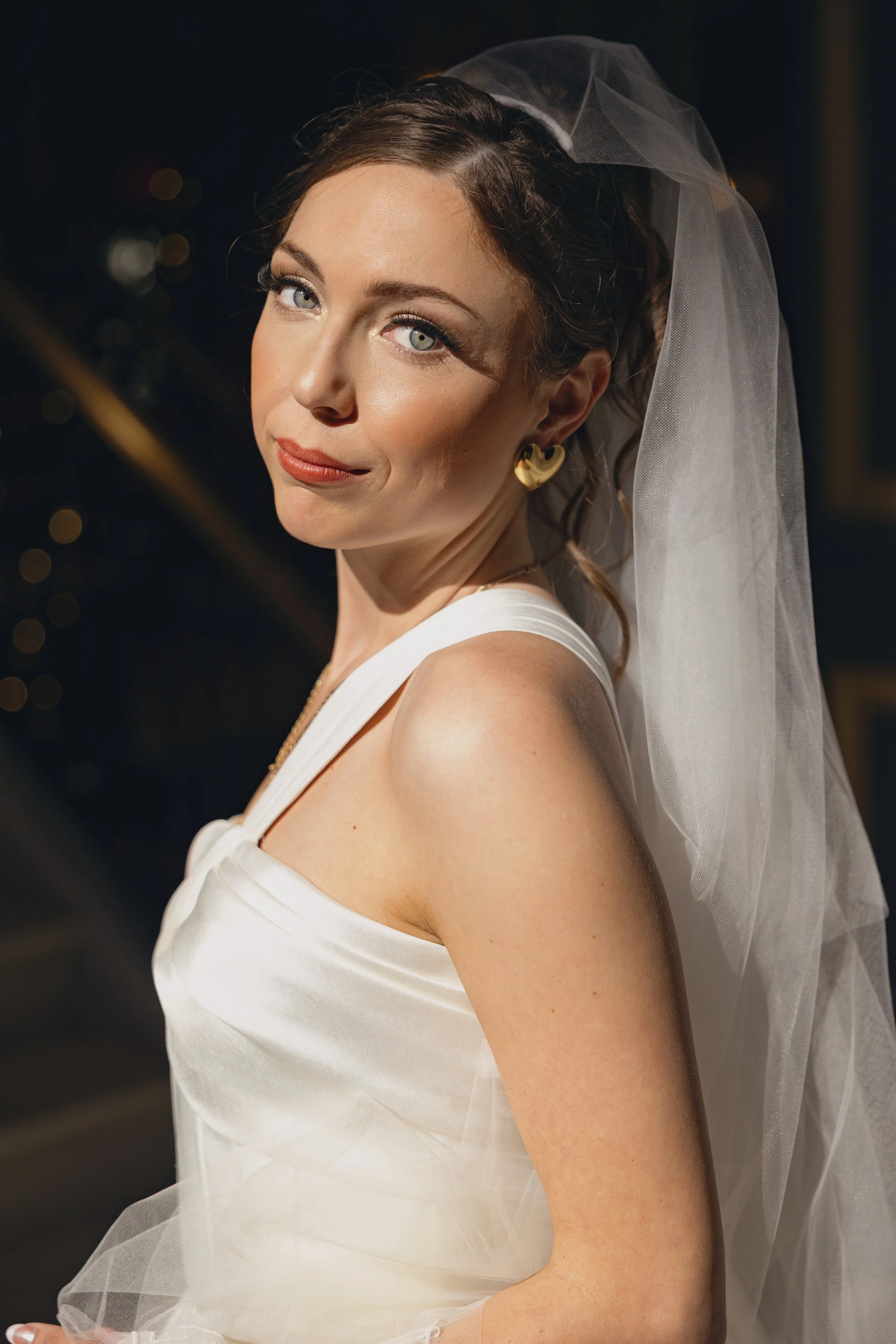 A woman in wedding attire with a white dress and veil, looking at the camera with a confident expression.