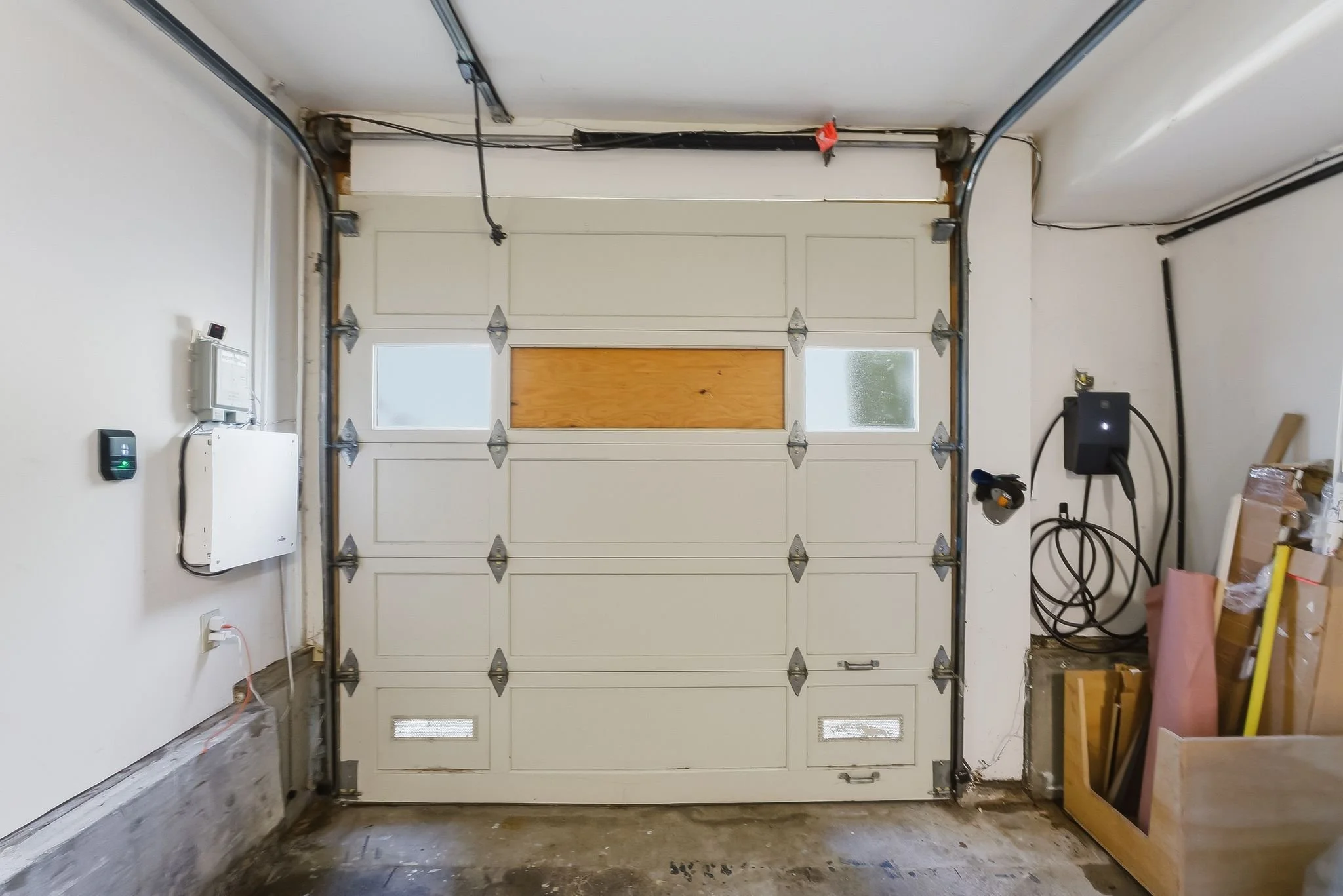 White garage door with windows, partially open, in a residential garage with various tools and boxes on the floor.
