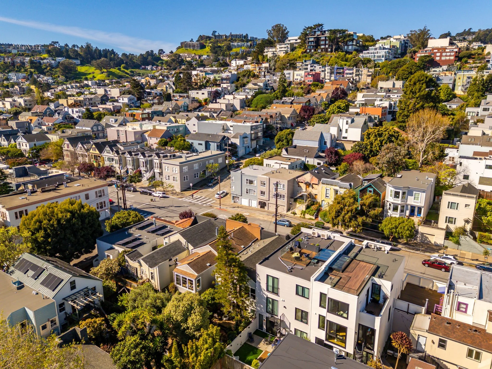 Aerial view of a hillside neighborhood with dense houses, trees, and streets in a sunny, urban area.
