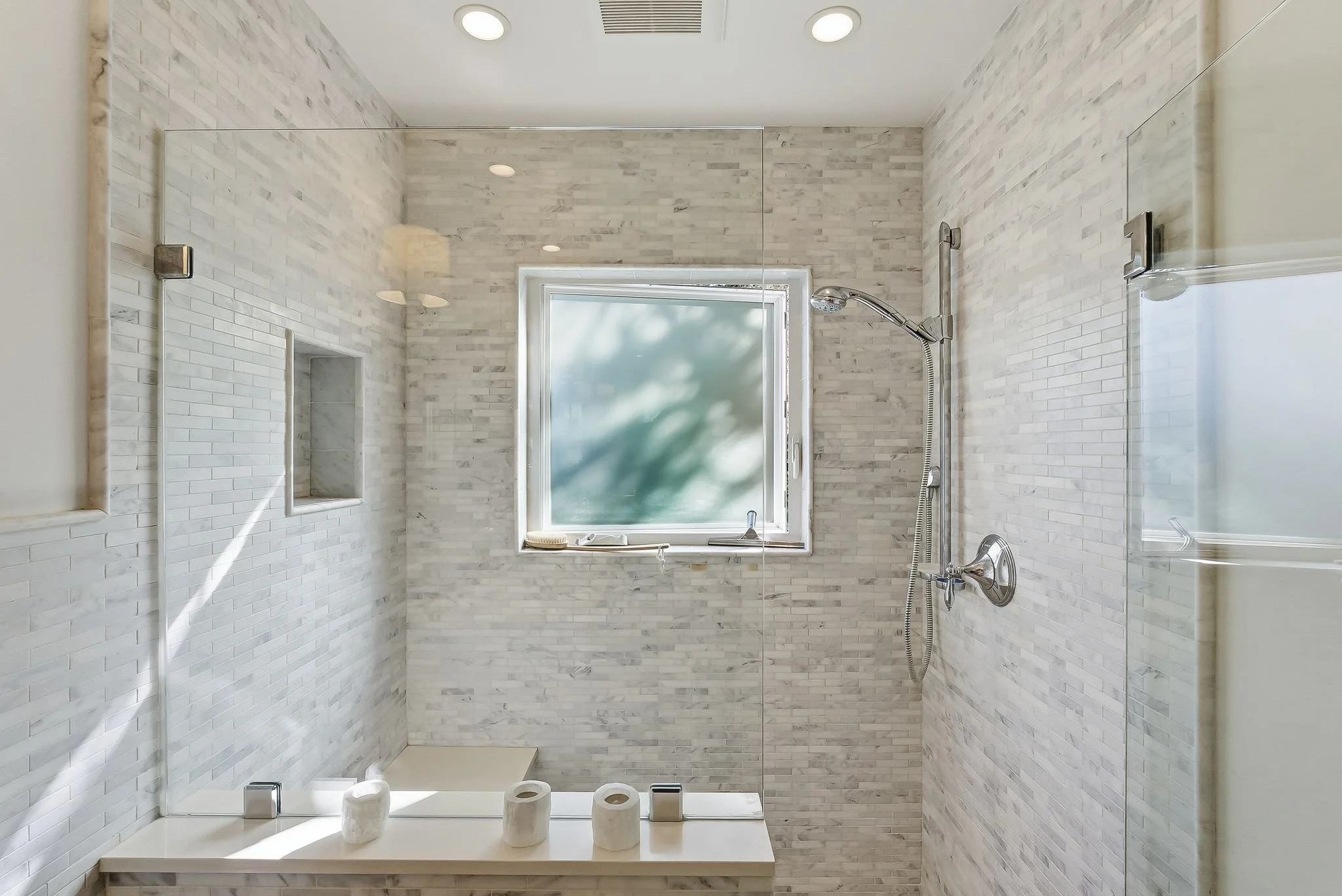 Modern shower with white subway tile walls, a frosted window, and three white candles on a marble ledge.