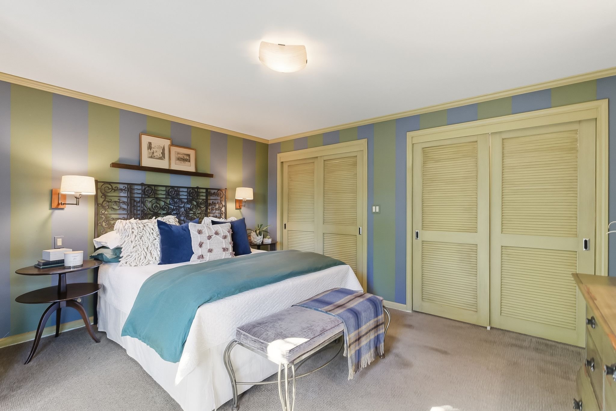 A bedroom with a bed, colorful striped walls, and closed closet doors.
