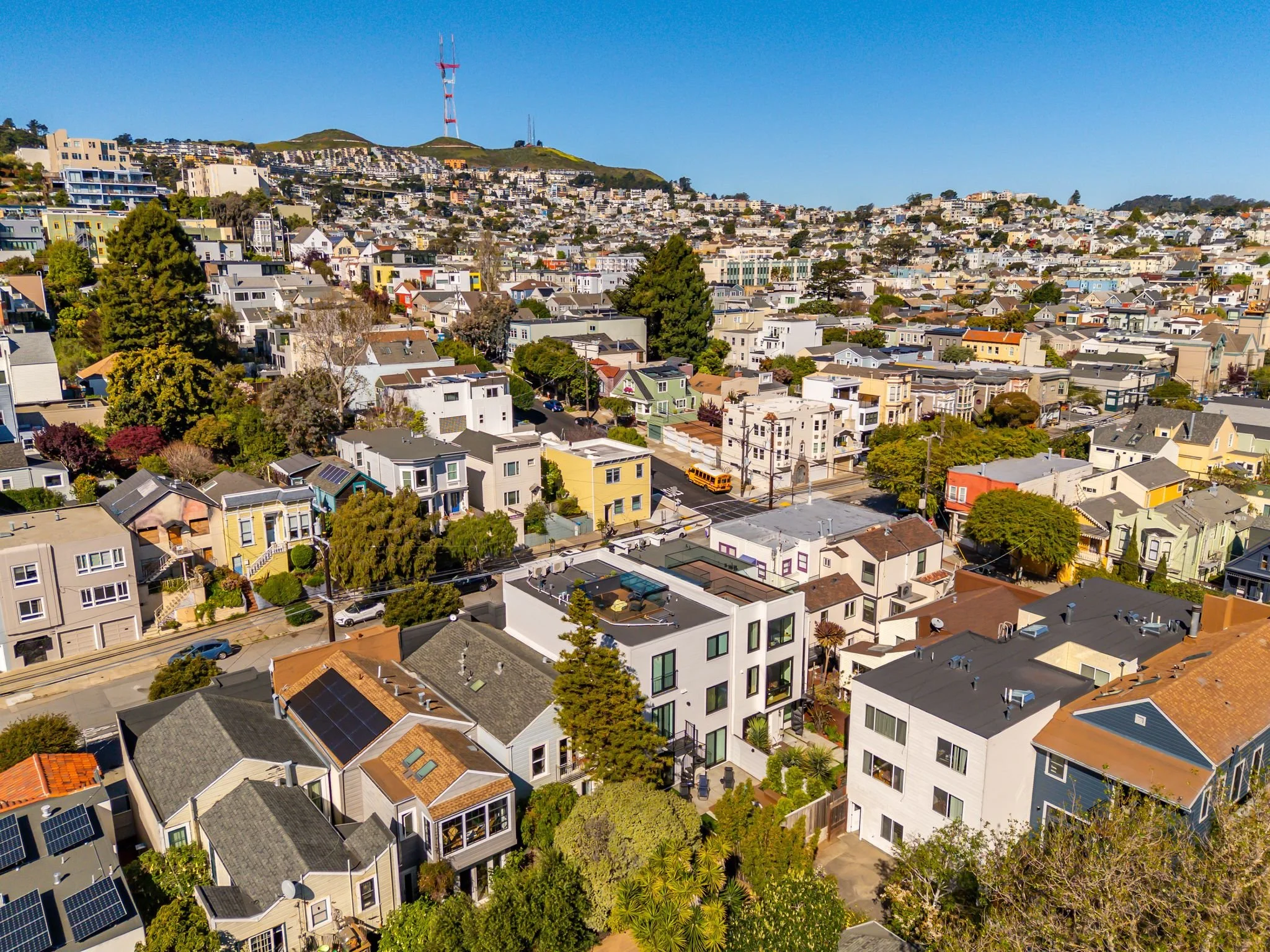 Aerial view of a hillside residential neighborhood with colorful houses, trees, and a radio tower on a hill in the background.