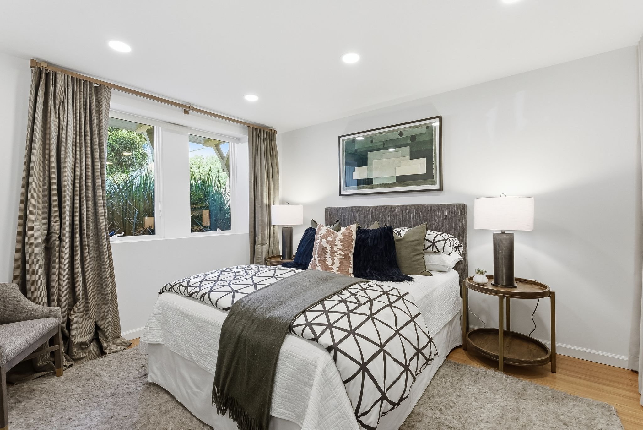 Bedroom with a bed, window with curtains, and two bedside tables with lamps.