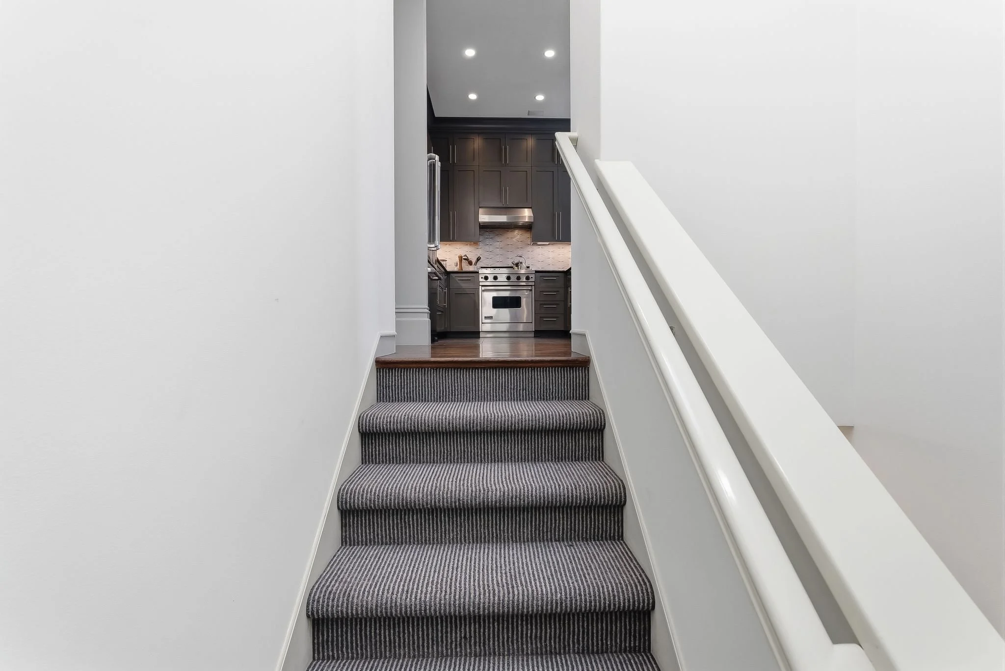 Carpeted stairs leading up to a kitchen with dark cabinets and stainless steel appliances.