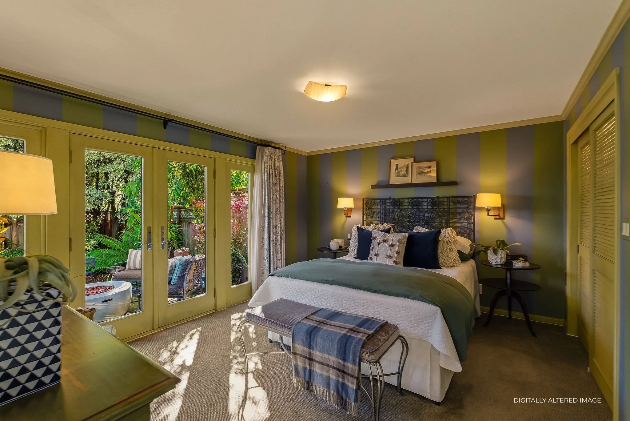 A bedroom with a large bed, nightstands, wall lamps, and French doors leading to a garden patio with outdoor furniture.