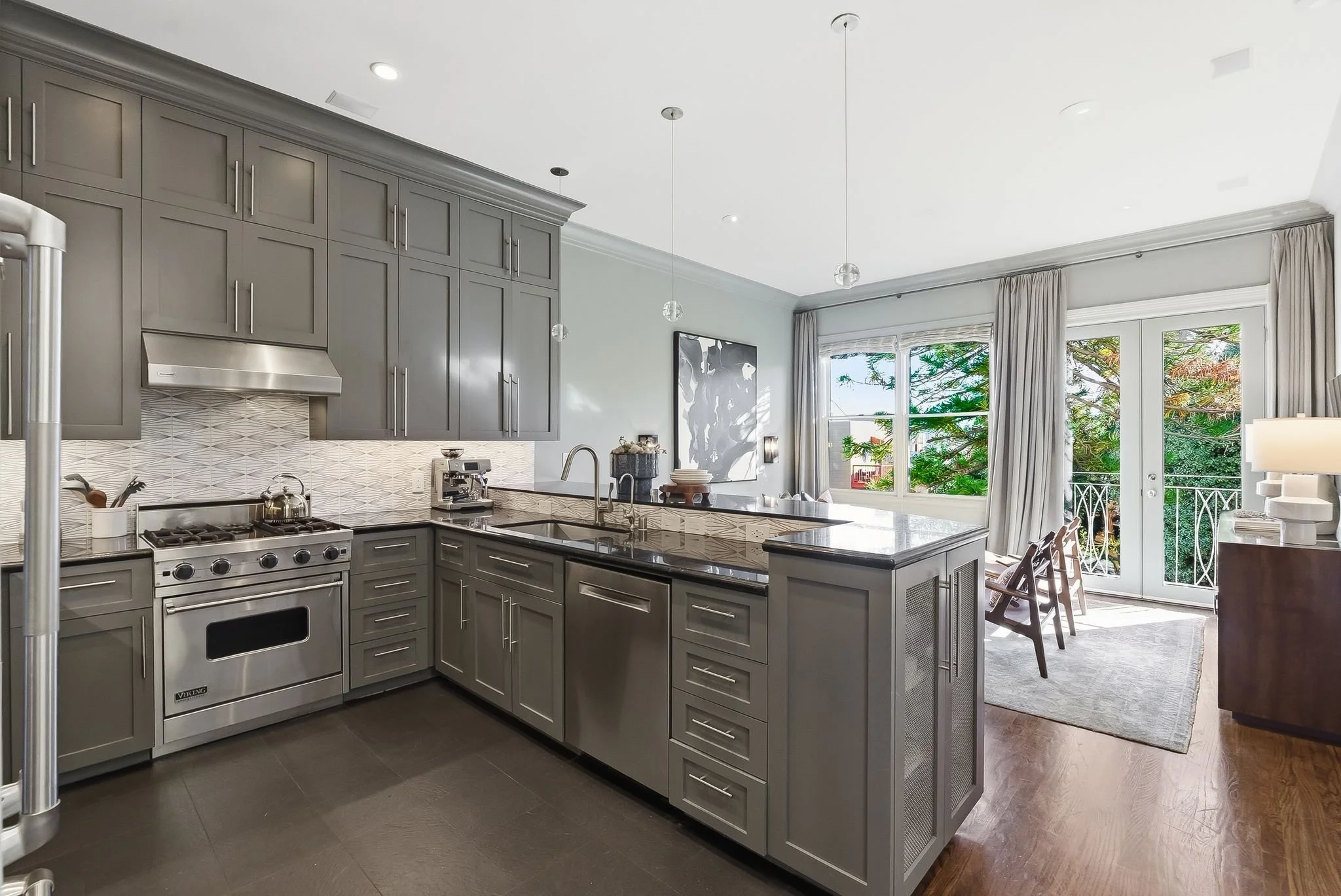 Modern kitchen with gray cabinets, stainless steel appliances, marble counter island, and large window with outdoor view.