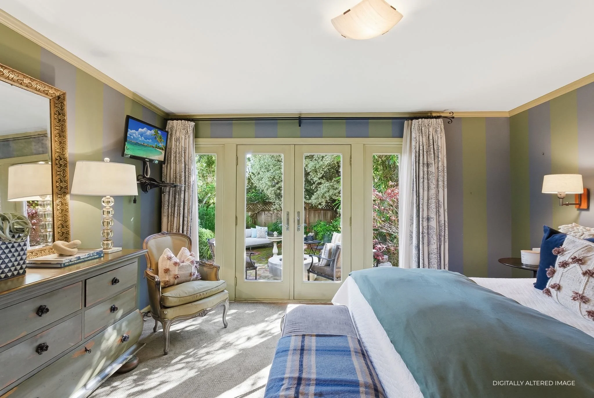 A bedroom with a bed, a dresser, and a view of a patio garden through glass doors.