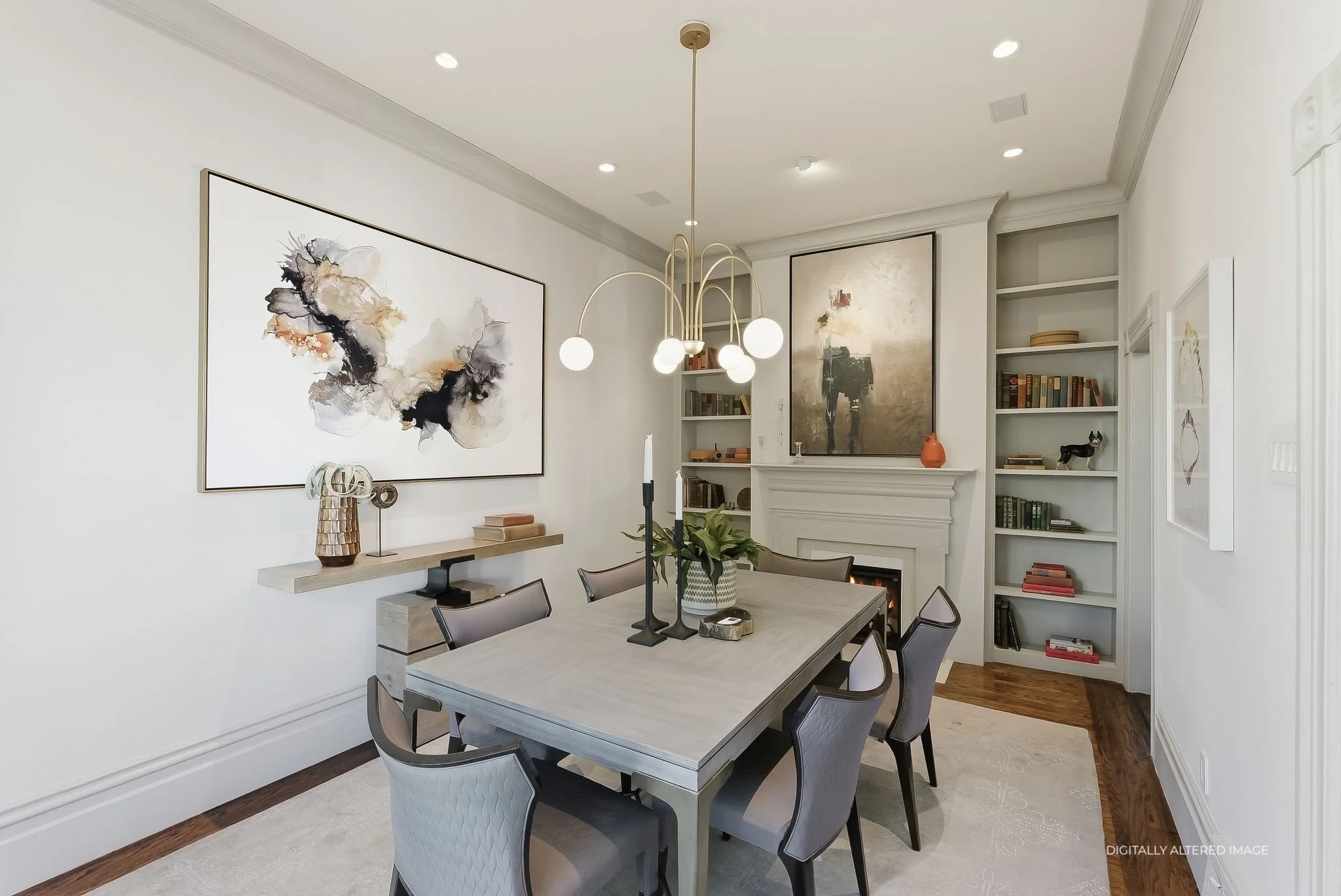 Modern dining room with white walls, hardwood flooring, a rectangular dining table with six chairs, a chandelier, abstract artwork on the walls, built-in shelves with books, and a fireplace.