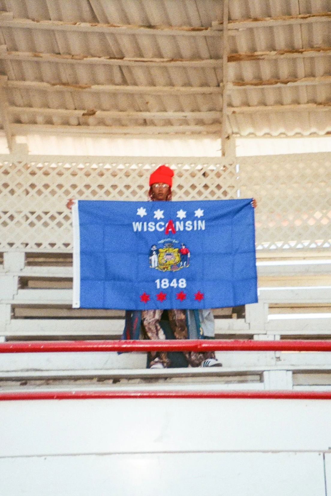 Person wearing a red hat holding a Wisconsin state flag.
