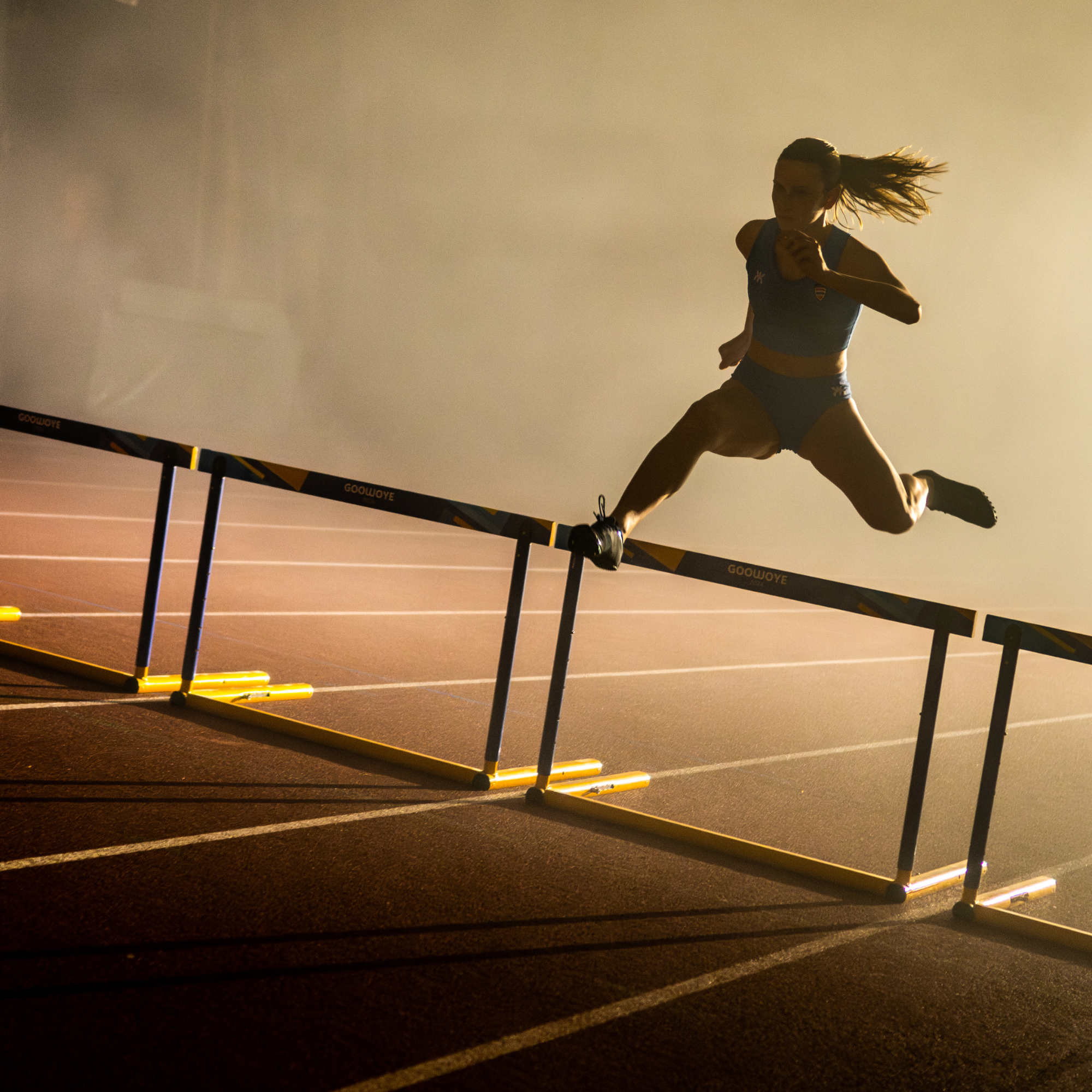 Athlete in mid-air jumping over hurdles on a track during a training session.