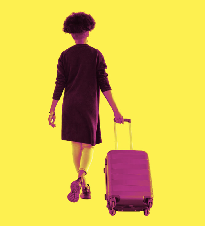 Person walking away with a rolling suitcase against a yellow background.