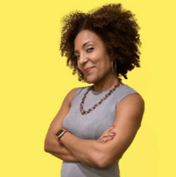 A confident woman with curly hair, wearing a gray sleeveless top, standing with crossed arms against a yellow background.