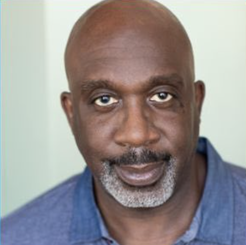 Close-up photo of an older African American man with a bald head and gray beard, wearing a blue shirt.