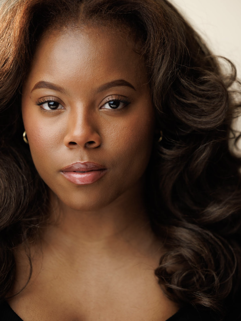 Close-up portrait of a Black woman with voluminous curly hair, wearing subtle makeup and hoop earrings.