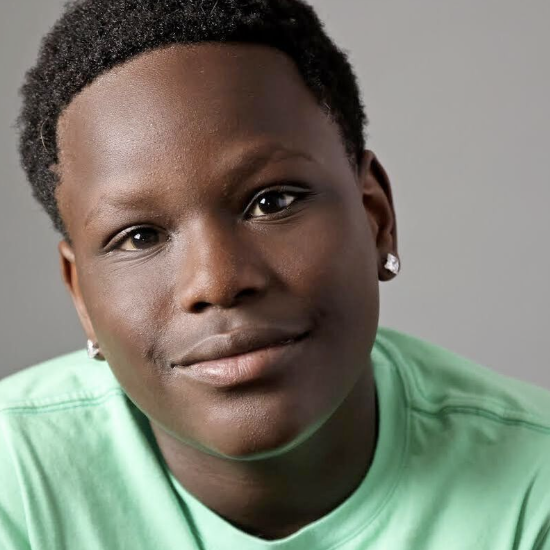 Close-up portrait of a young person with short curly hair, wearing diamond earrings and a mint green shirt, looking at the camera with a slight smile.
