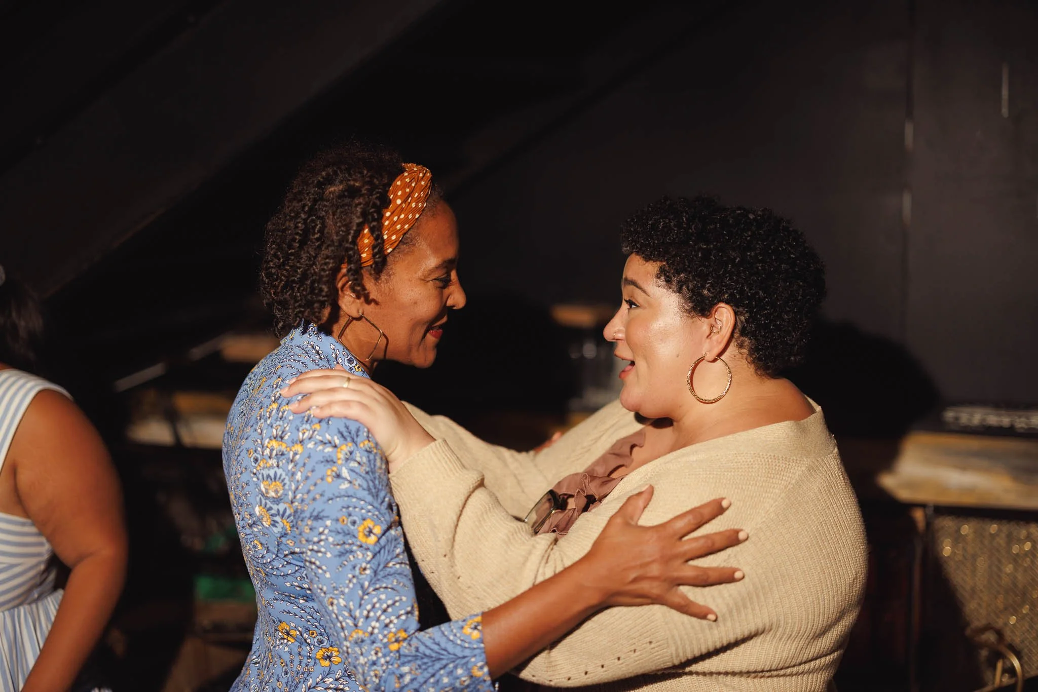 Two women with curly hair smiling and embracing each other in a close, happy moment.