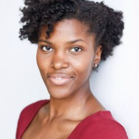A young woman with natural curly hair, wearing a red top, smiling softly at the camera.