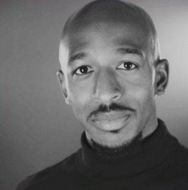 Black and white portrait of a man with a bald head and a slight mustache, wearing a dark turtleneck sweater.