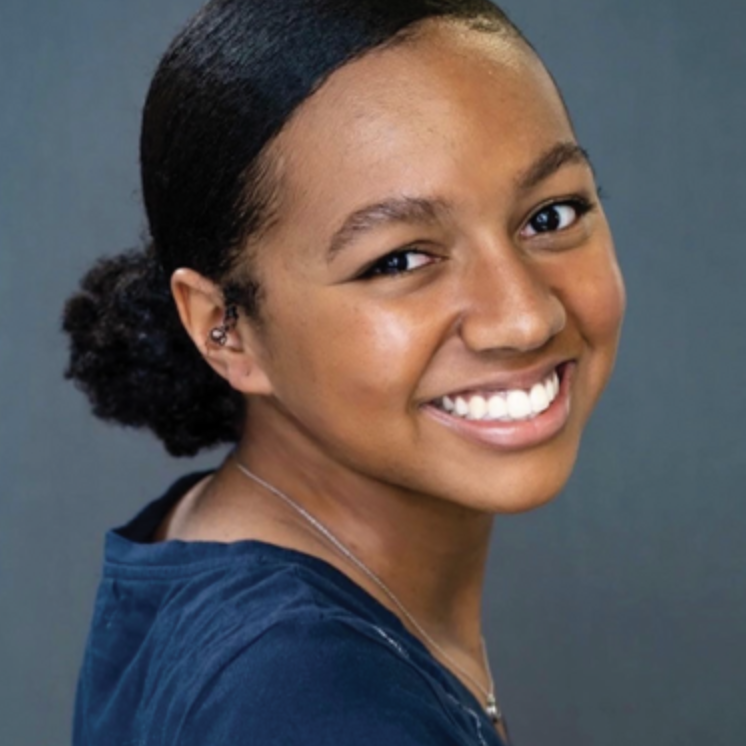 Portrait of a young woman with a smile, dark hair pulled back, wearing a dark top, against a plain background.