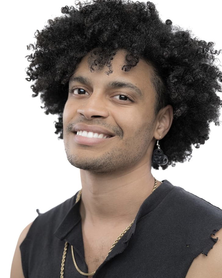 A young man with dark curly hair smiling at the camera, wearing a sleeveless black shirt, gold necklace, and earring with a skull pendant.