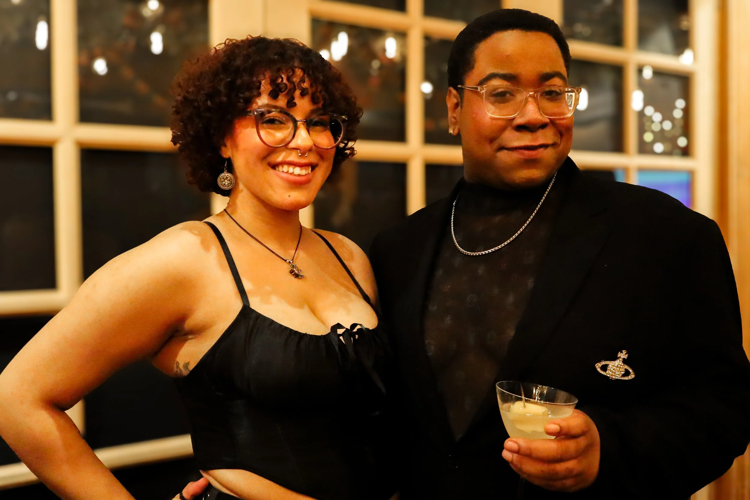 Two people posing together at a social event, one person holding a cocktail.