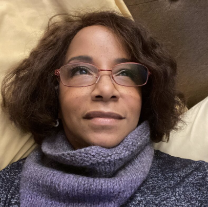 Woman with short curly hair wearing glasses and a purple scarf, lying on a couch.