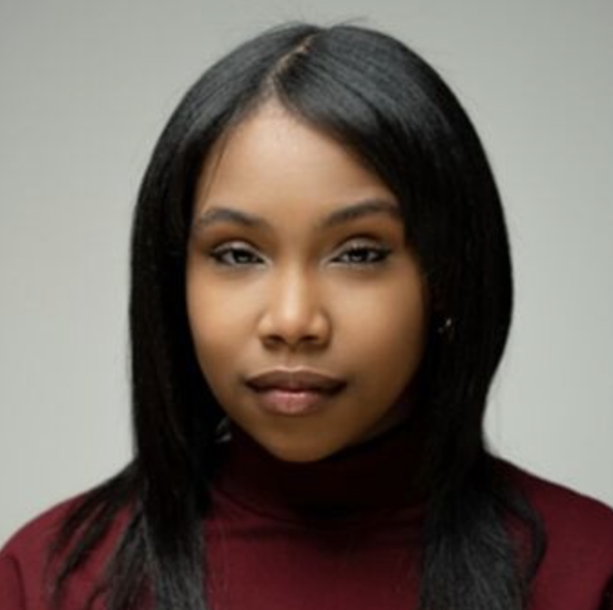 A young woman with straight black hair wearing a maroon turtleneck against a plain background.